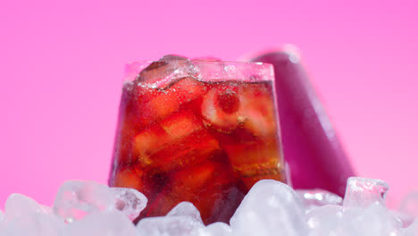 Nahaufnahme-Eines-Gekühlten-Kaltgetränks-Im-Glas,-Das-Aus-Der-Dose-Auf-Eiswürfel-Vor-Rosa-Hintergrund-Gegossen-Wird